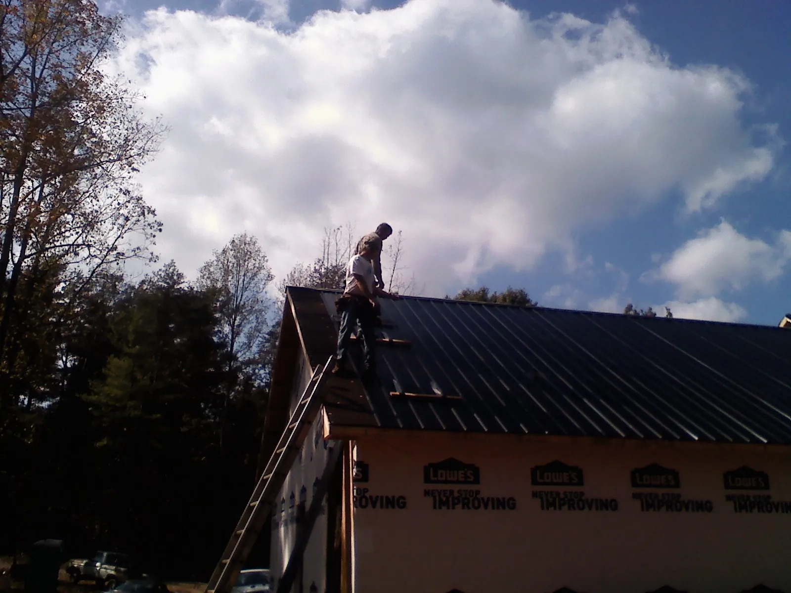 Roofer fastening dark metal panels high against a cloudy sky, from a Roof Inspection job in Eden